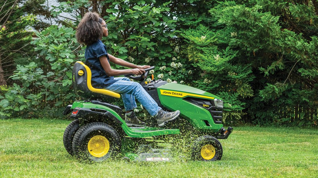 A photo of a John Deere S160 Ride-On Mower being driven by a woman and cutting the lawn.