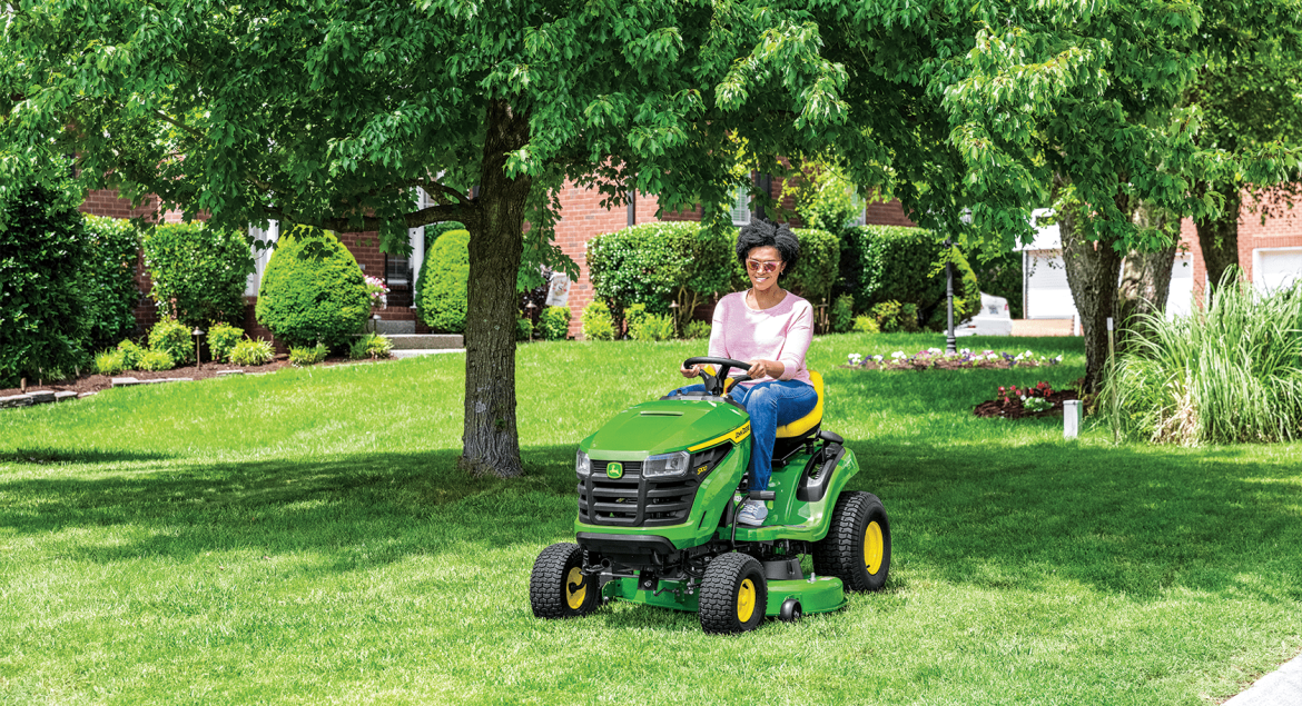 A photo of a John Deere S-series Ride-On Mower with a person driving it to cut a big piece of lawn.
