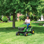 A photo of a John Deere S-series Ride-On Mower with a person driving it to cut a big piece of lawn.