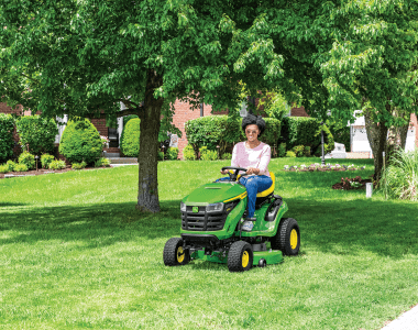 A photo of a John Deere S-series Ride-On Mower with a person driving it to cut a big piece of lawn.