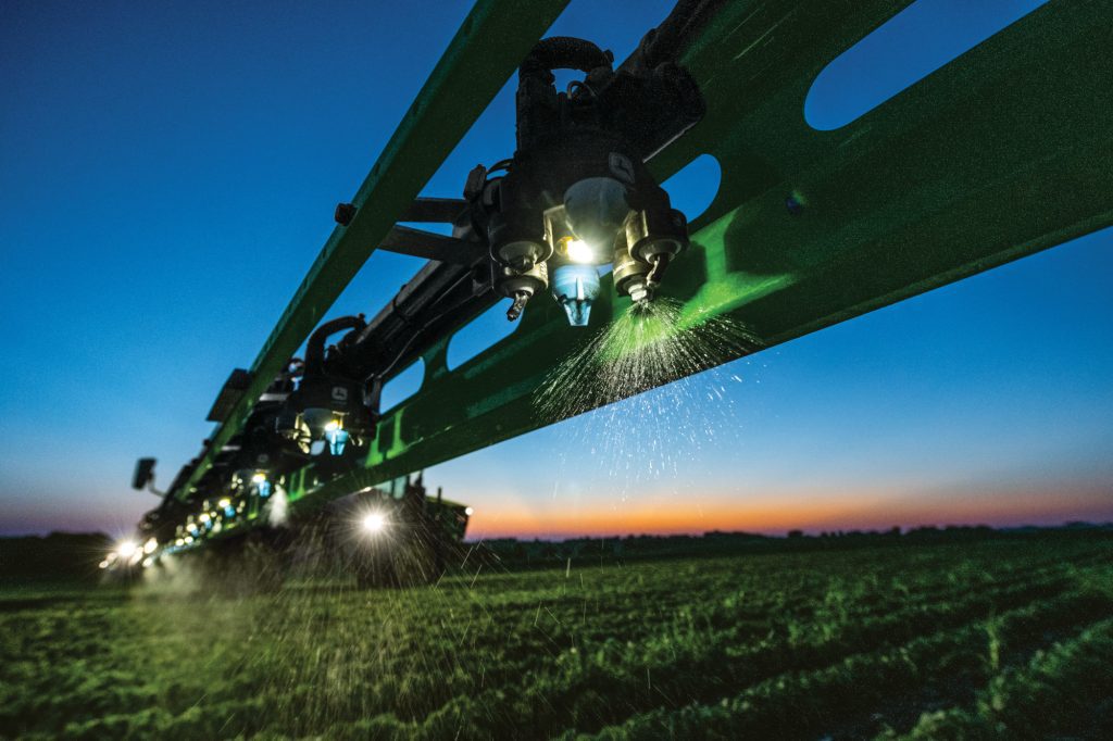 A John Deere 412R Self-Propelled Sprayer driving in the Night with Lights on.