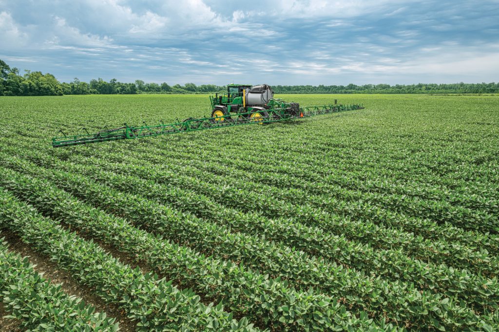 A photo of a John-Deere-612R-Self-Propelled-Sprayer In a green Field as it sprays