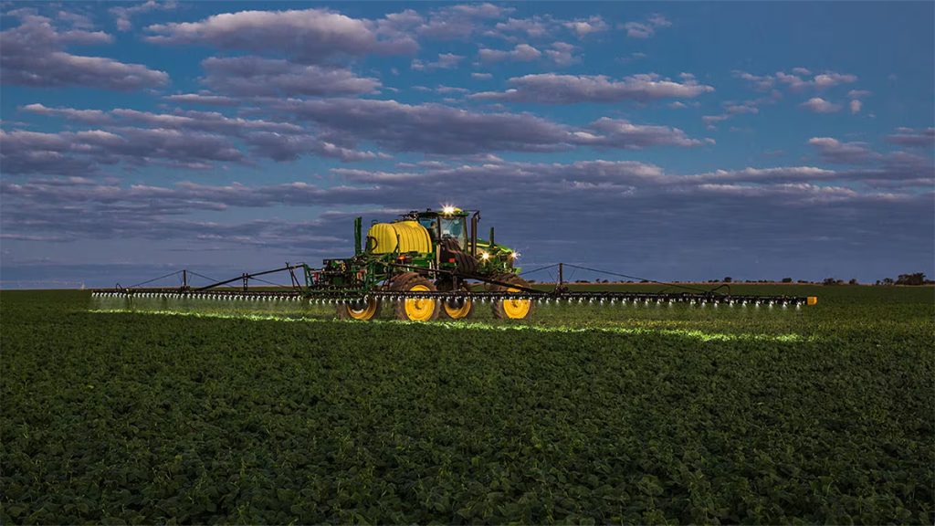 John Deere M4030 sprayer operating at dusk, showcasing advanced guidance and nozzle control technology for consistent coverage.