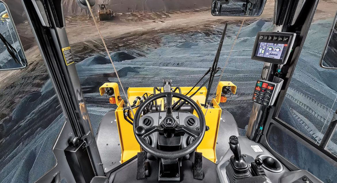 View from inside a John Deere construction machine cab showing modern controls and a wide view of the job site.