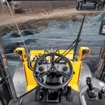 View from inside a John Deere construction machine cab showing modern controls and a wide view of the job site.
