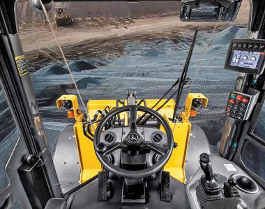 View from inside a John Deere construction machine cab showing modern controls and a wide view of the job site.