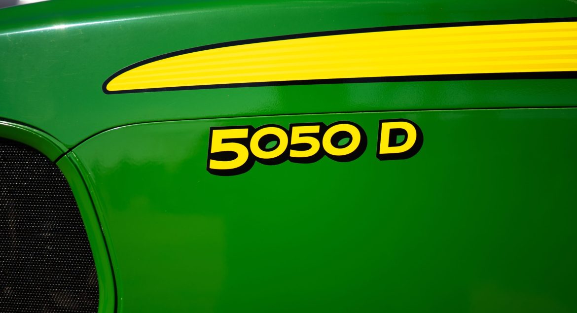 A photo of a close-up of the front nose of a John Deere 5050D tractor showing the tractor name with the John Deere green