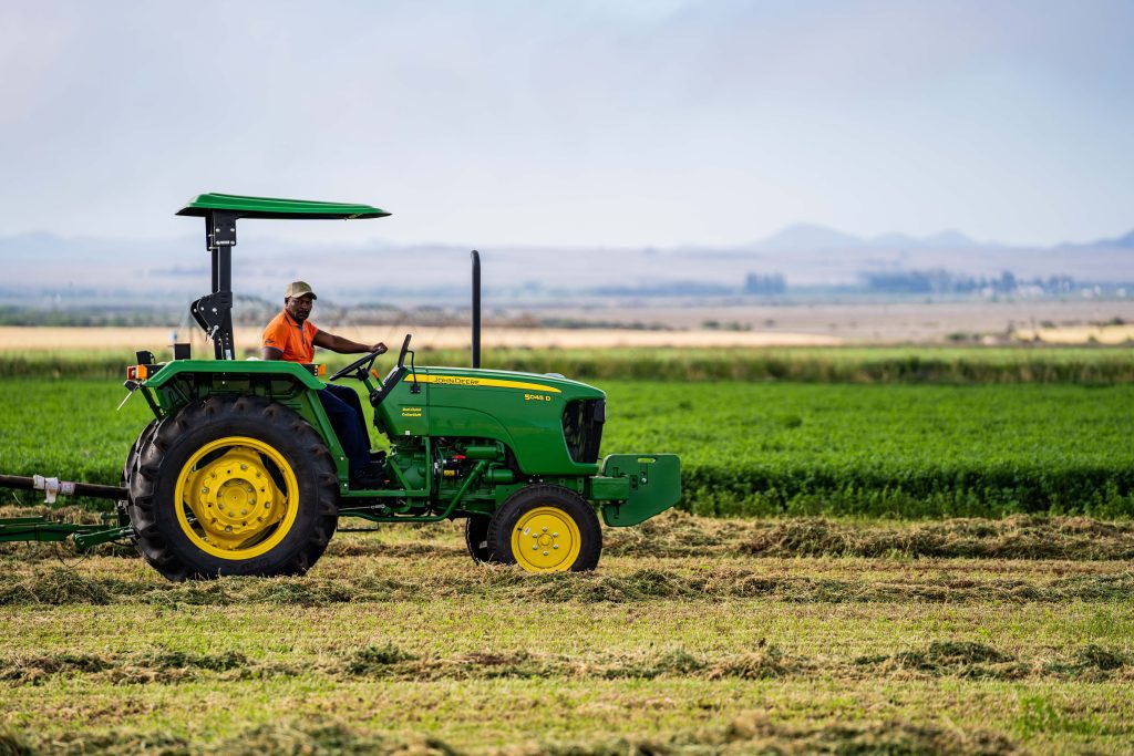 A photo of a John Deere 5050D tractor working in the filed as it's pulling a baler to create hay bales.