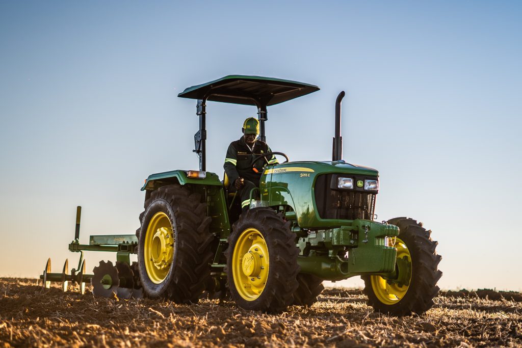A photo of a John Deere 5055E tractor working in the filed as it's pulling an implement to work the field.