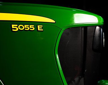 A photo of a close-up of the front nose of a John Deere 5055E tractor showing the tractor name with the John Deere green