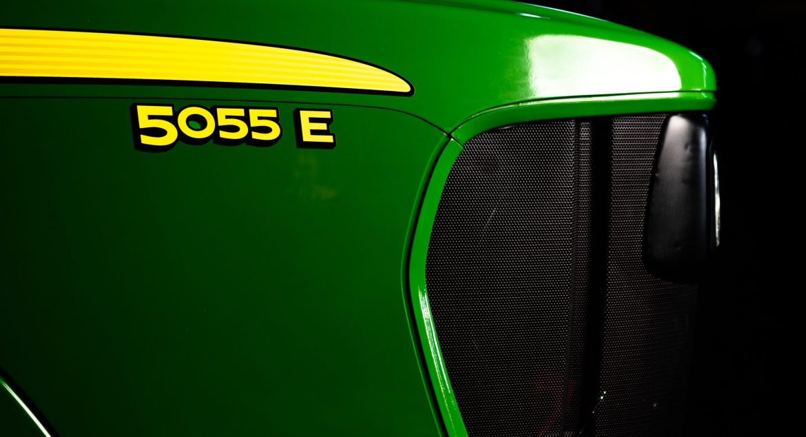A photo of a close-up of the front nose of a John Deere 5055E tractor showing the tractor name with the John Deere green