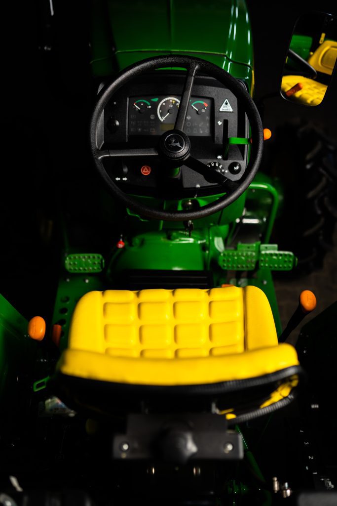 A photo of a yellow, adjustable deluxe vinyl seat that comes standard in the John Deere 5E Series tractors with its controls.