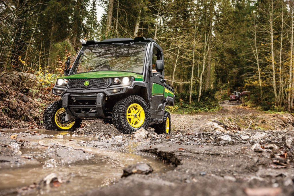 John Deere diesel utility vehicle driving on gravel road with some water present