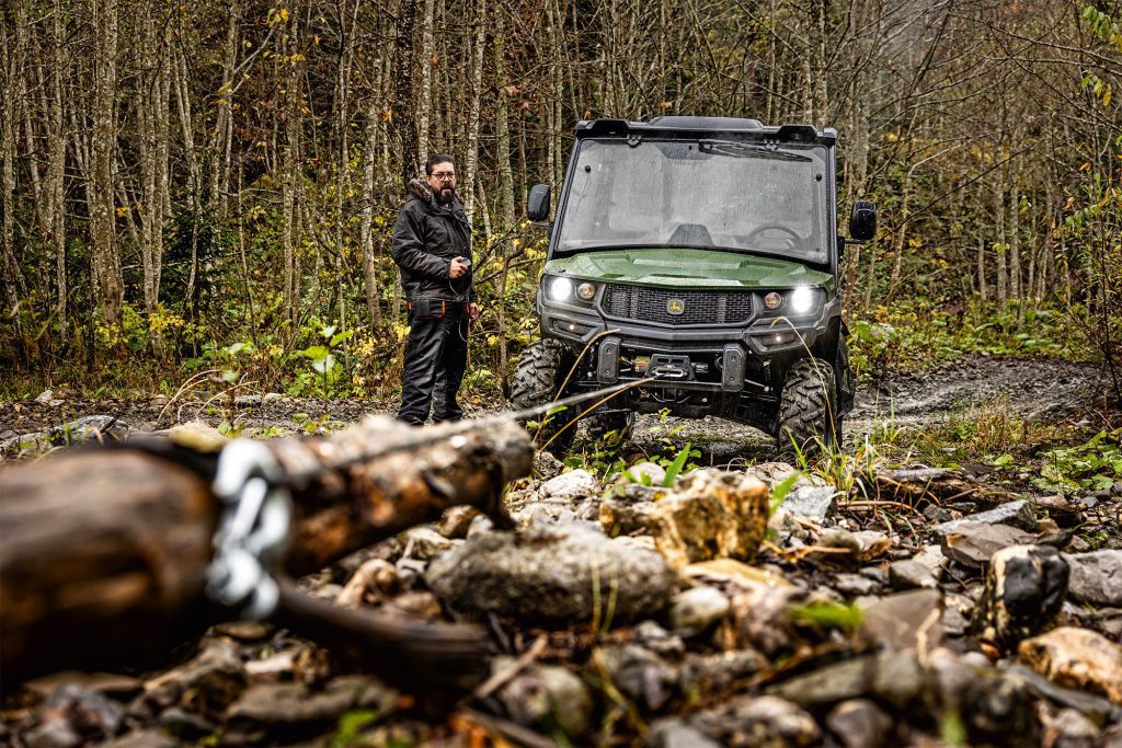 A photo of a John Deere XUV 875M pulling a piece of log on an estate or farm to clear the debris