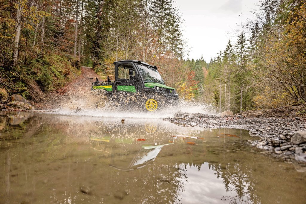 A photo of the John Deere XUV 875M Diesel as it drives through a stream, splashing water and showing its durability.