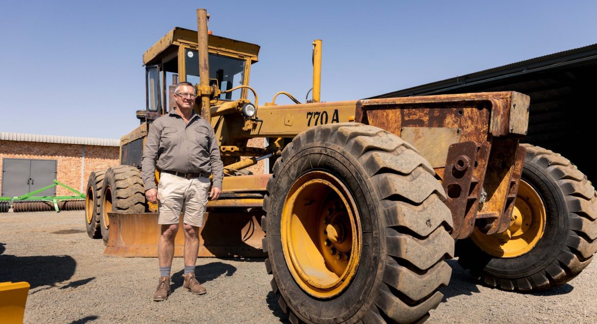 Photo of the old John Deere 770A Motor Grader with a representative of Elite Guys