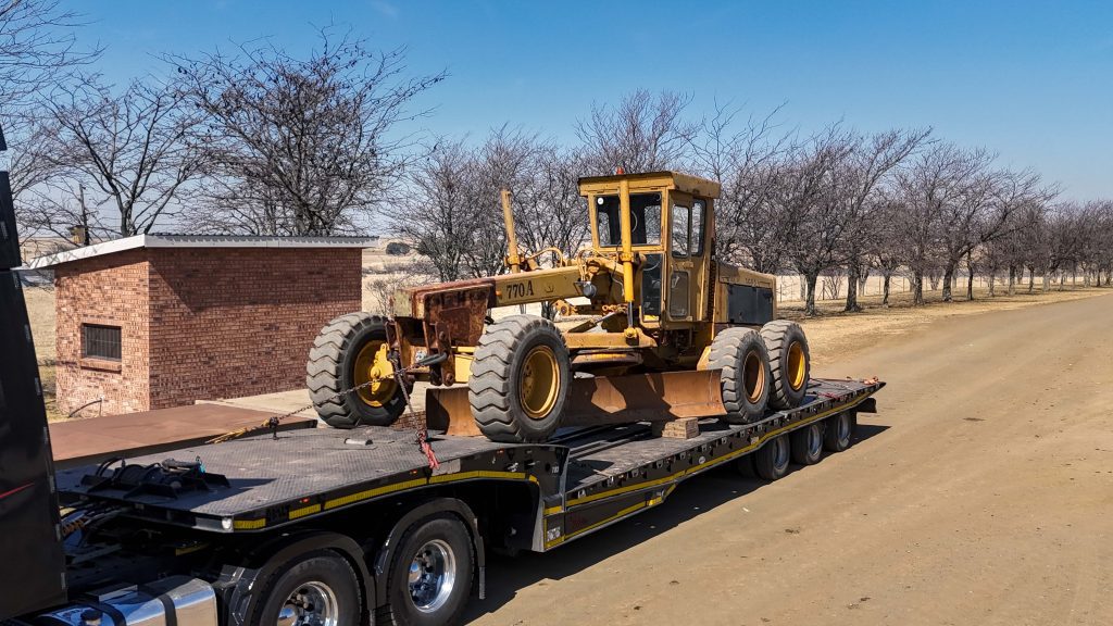 Old John Deere 770A Motor Grader on back of loading truck.