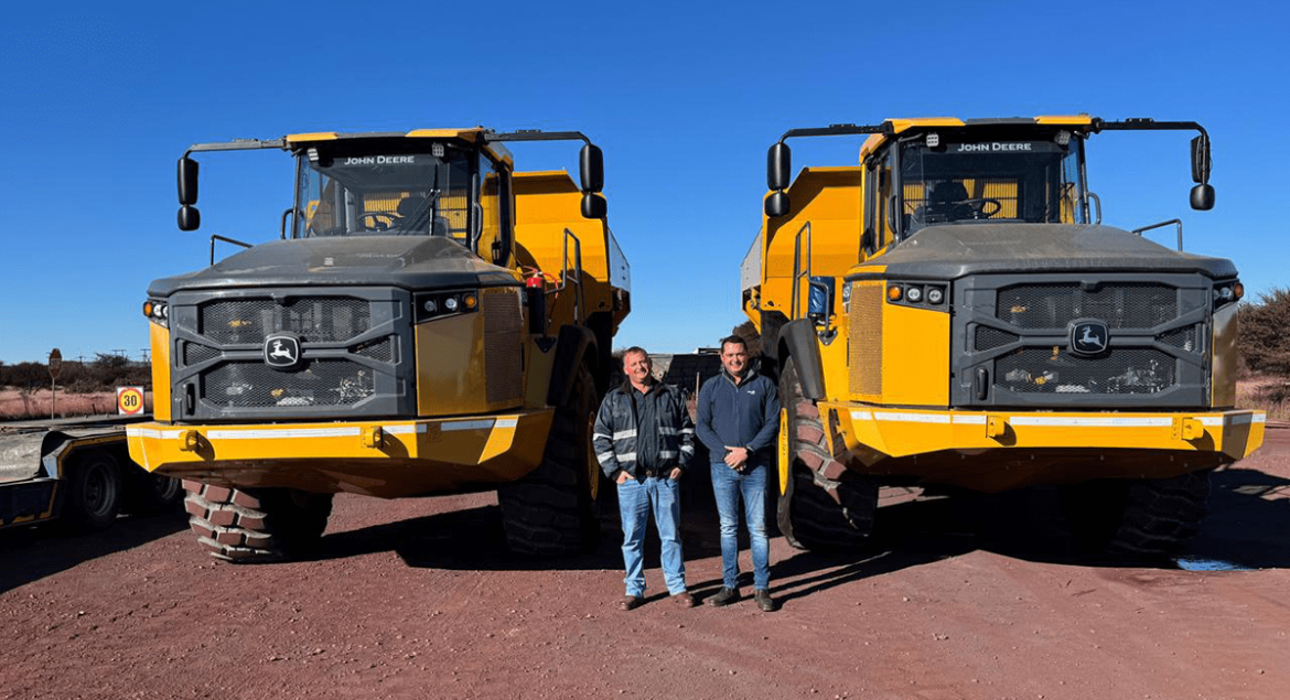 Jaco Botes from Moshaweng Mining & Drilling with an AFGRI Equipment representative standing in front of two articulated dump trucks (ADTs) on site, showcasing John Deere mining equipment.
