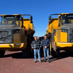 Jaco Botes from Moshaweng Mining & Drilling with an AFGRI Equipment representative standing in front of two articulated dump trucks (ADTs) on site, showcasing John Deere mining equipment.