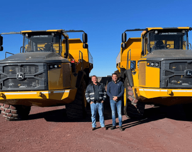 Jaco Botes from Moshaweng Mining & Drilling with an AFGRI Equipment representative standing in front of two articulated dump trucks (ADTs) on site, showcasing John Deere mining equipment.