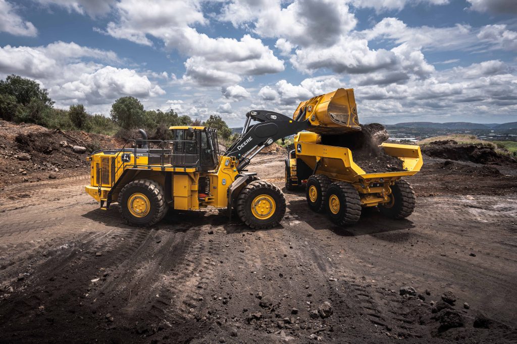 Photo of two John Deere machines, one ADT and one Wheel Loader where the loader is dropping some sand in the ADT's bucket