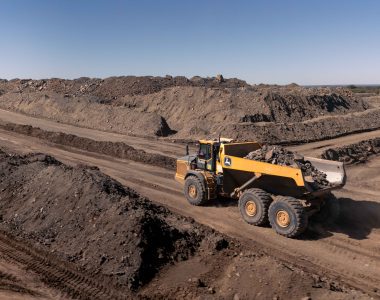 A John Deere 460 P-Tier Articulated dump truck transporting material across challenging mining terrain.
