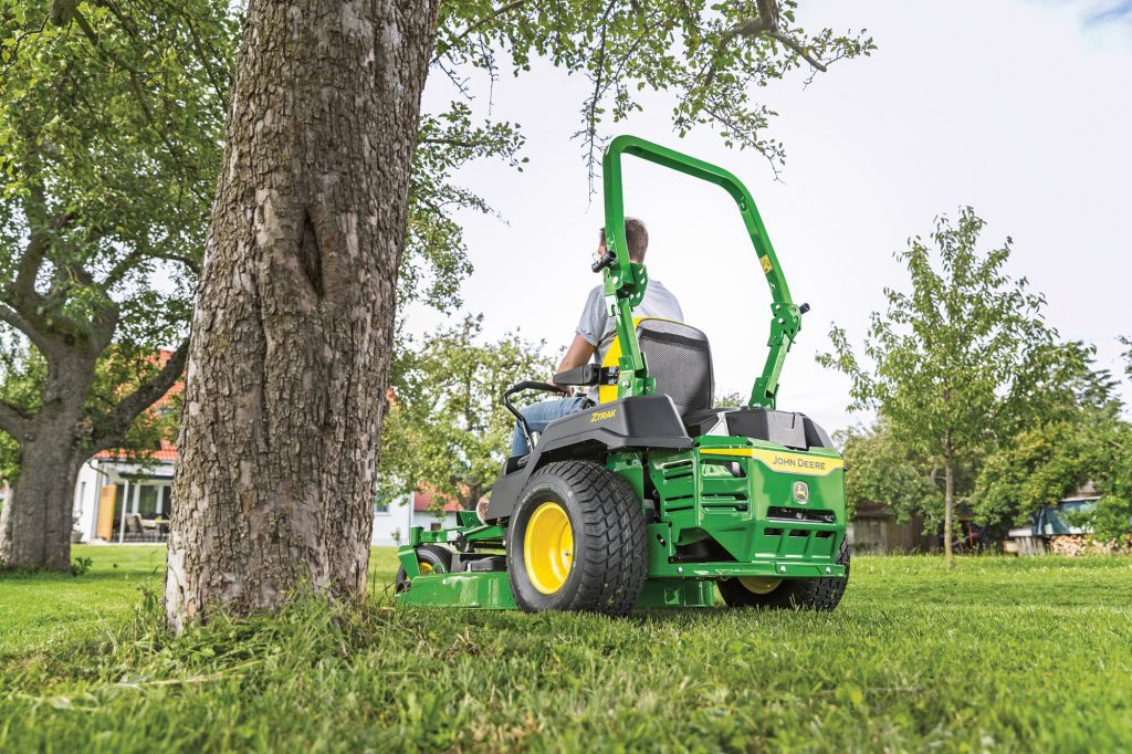 John Deere ZTrak zero turn mower maintaining large estate grounds and doing tight turns around a tree.