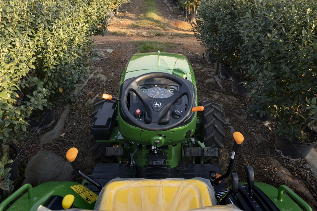 John Deere 3036EN tractor standing between fruit trees, showing the nose, steering and other control levers. The photo is taken from an operator's POV.